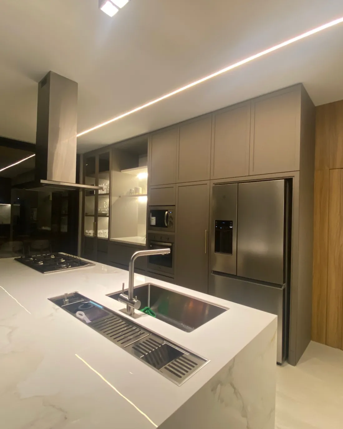 Cozinha com ilha central em pedra, cuba integrada e iluminação linear embutida