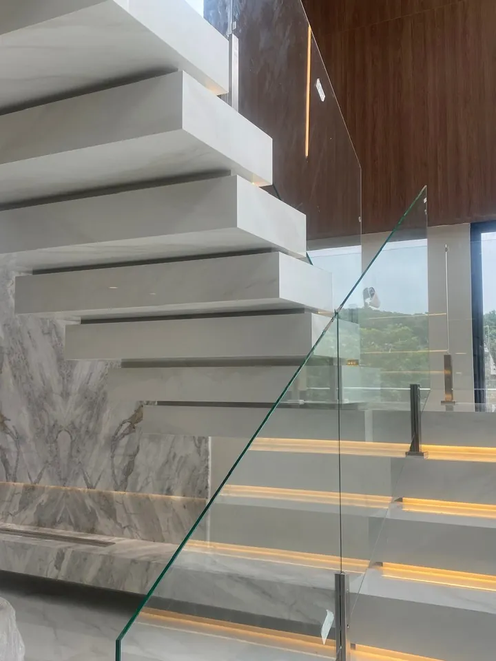 Escada de degraus em balanço com guarda-corpo de vidro e parede de mármore