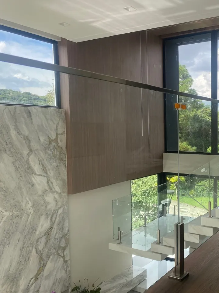 Mezanino de pé-direito duplo com parede de mármore, piso de madeira e vista para a mata